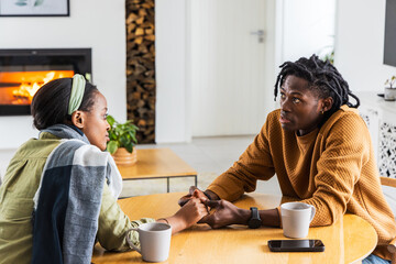 Naklejka premium African American couple holding hands talking at round table in living room with phone watch