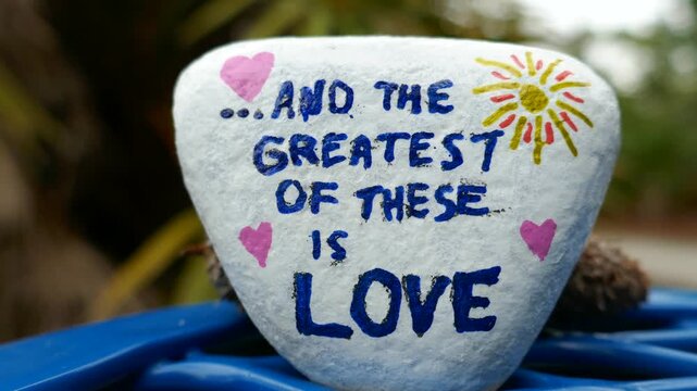 And the greatest of these is love kindness rock close-up with blurred motion background