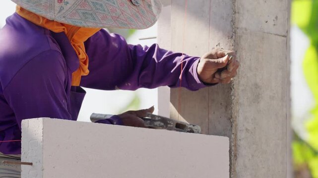 Professional mason carefully placing concrete block with mortar for structural wall construction. Detailed building craftsmanship in industrial construction environment outdoors.