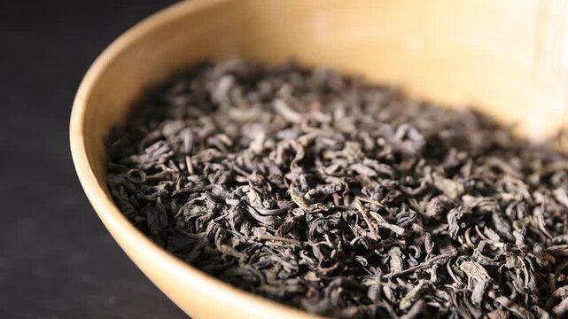 Pouring dried tea leaves into bowl against dark background, closeup