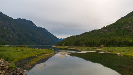 Obraz premium Strathcona Provincial Park's Buttle Lake shoreline with sandbars and mirrored mountain views on a cloudy day.