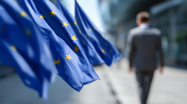 European Union flags waving outdoors with a blurred man in a suit walking away in a modern urban setting, symbolizing politics and international relations