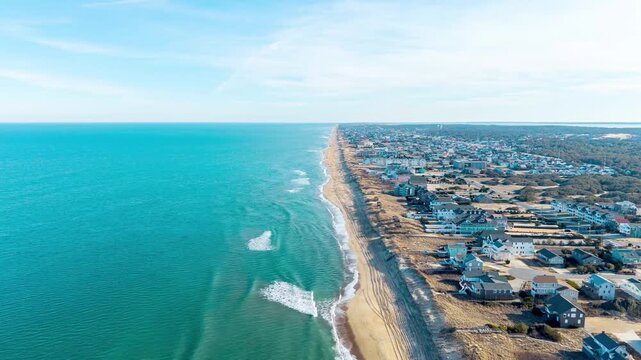 Kill Devil Hills, North Carolina, an aerial hyperlapse flying along the Atlantic coastline showing beachfront vacation rentals, sandy dunes, and turquoise ocean waters.