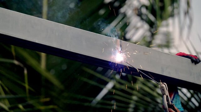 Metal fabrication welding process creating bright electric sparks on steel structure. Industrial construction and structural engineering concept in outdoor environment.