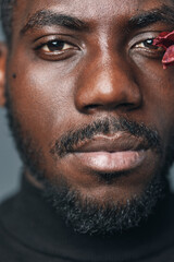Fototapeta premium African man portrait closeup with beard and mustache wearing black turtleneck in creative conceptual visual style with flower petal on face for artistic expression and diversity.