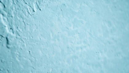 Abstract close-up of rough textured wall surface painted in pale cyan blue color. Uneven stucco texture background or architectural material backdrop.