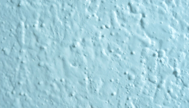 Rough textured wall surface painted in light pastel blue, featuring a bumpy stucco or popcorn ceiling finish pattern background and copy space.