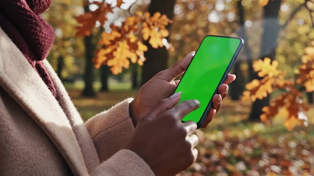 Green Screen woman holds mobile phone and swipes photos or pictures outside on a cold autumn day use vertical for copy space closeup chroma key mock up smartphone in hand surfing internet 4k scene 4