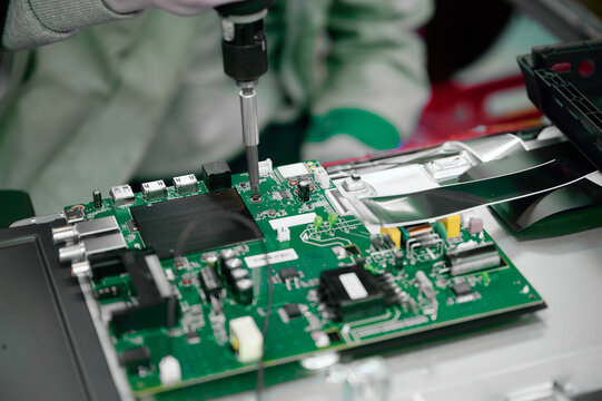 Workers assemble a circuit board at a television manufacturing plant focusing on precision and quality control