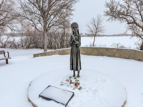 January, 2026 - Regina, Canada: Holodomor memorial monument depicting a solemn girl statue during snowfall, symbolizing famine remembrance and Ukrainian heritage.