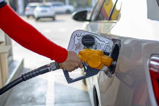 Person refuels car at gas station, holding yellow fuel nozzle. vehicle is parked at pump, and scene suggests routine refueling stop