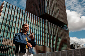 Tourist using smartphone app is waiting near hotel with suitcase