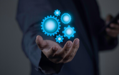 Businessman holding virtual gear mechanism with glowing blue light. Concept of business workflow, system automation, and strategic solution.
