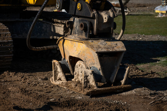 Closeup of excavator compactor attachment on fresh dirt on development construction job site
