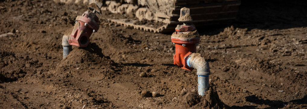 Newly installed water utility pipeline and backflow preventer in fresh dirt on development construction job site, tracked heavy equipment vehicle I background
