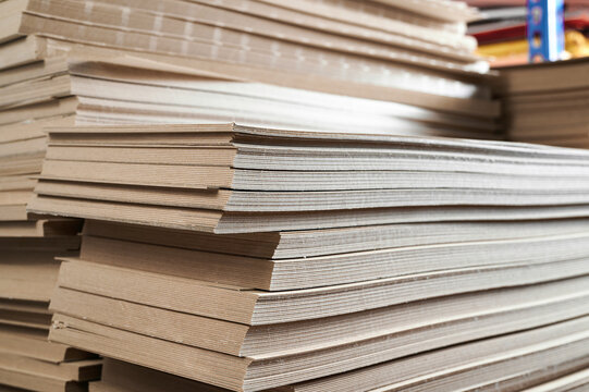 Stacks of thick paperboard await transformation into durable cardboard boxes in a bustling manufacturing facility