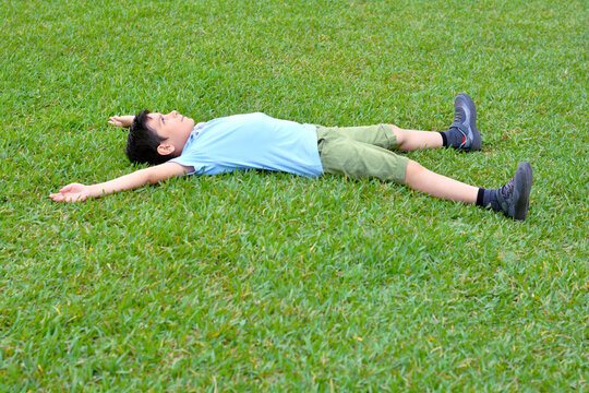 Latin boy laying on the grass in starfish pose.