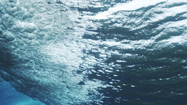 Underwater wave surface with rippling light and drifting bubbles forming abstract ocean texture