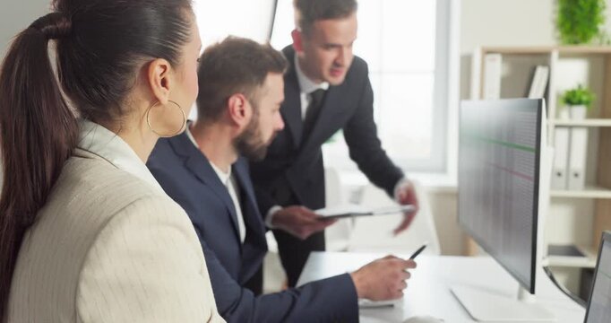 Team colleagues in office meeting analyze data. The manager gestures at the computer as the business group reviews analysis and aligns strategy toward goals. Clear teamwork and leadership.