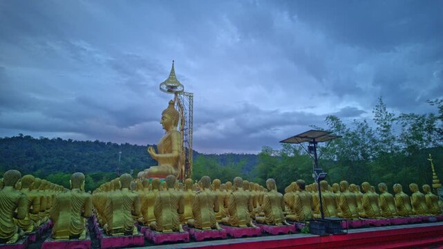 The grand Ovāda Pātimokkha Buddha image dominates the grounds, with rows of small statues creating a powerful visual of unity and faith Serene Golden Buddha Statue Against Dramatic Cloudy Sky