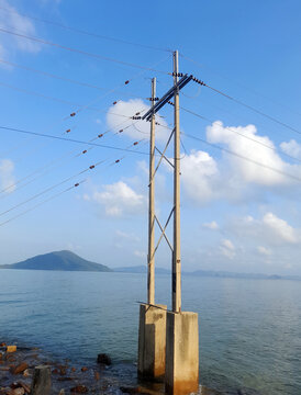 Electric lines hum over a quiet sea as a lone island waits on the horizon