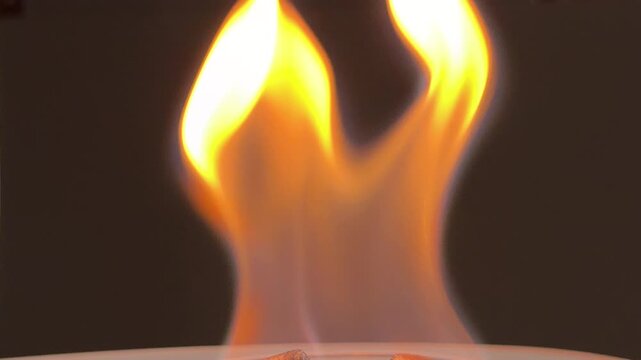 White chemical fuel tablets burn intensely inside a glass tray. The large, vibrant orange flame dances against a dark background. This combustion creates quiet crackling and flickering pops.