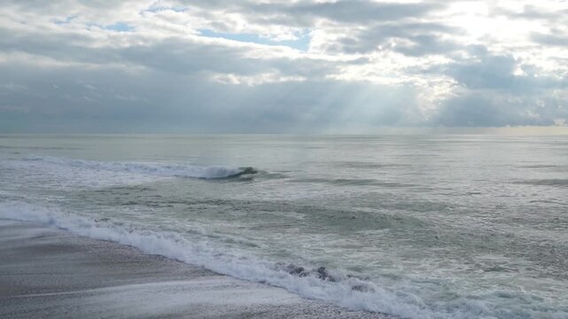 Dramatic Ocean Waves Under Cloudy Sky with Sun Rays