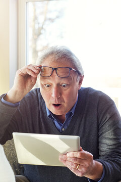 Glasses, tablet and wow with senior man in living room of home for notification or reaction. App, reading and surprise with old person in apartment for alert, retirement payout or shocked expression