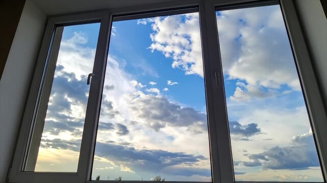 A multi-pane window reveals a vibrant blue sky filled with puffy, dramatic clouds