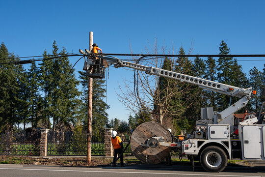 Power utility lineman in an aerial lift bucket upgrading utilities by replacing power lines and communication cable with fiber optics, work truck with cable spool
