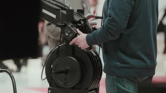 Crew member adjusting cable reel on studio camera crane during setup