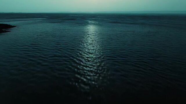 Ocean surface of gentle ripples catching warm sunlight, creating a serene, expansive seascape under a clear sky with soft clouds and tranquil reflections
