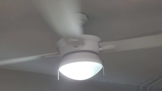 White ceiling fan spinning overhead mounted on the ceiling. The rapid rotation provides airflow and cooling for indoor comfort.
