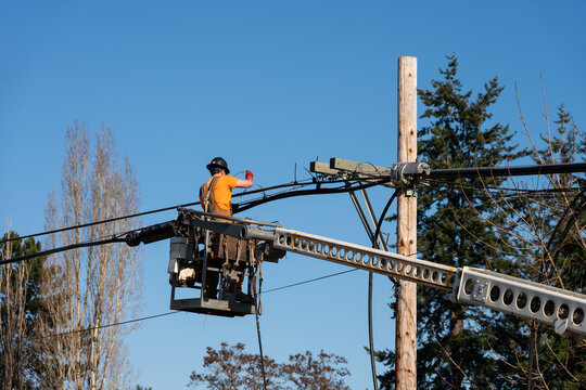 Power utility lineman in an aerial lift bucket using a Cable Lasher to upgrade utilities by replacing power lines and communication cable with fiber optics
