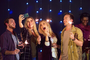 Friends, sparklers and selfie at nightclub for party with drinks, celebration or excited on new years eve. People, group and happy at event with photography, alcohol and post memory on social network