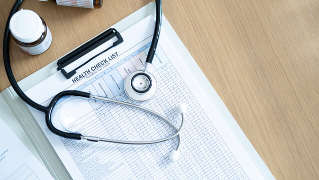 Top view stethoscope on health checklist report on wooden table, concept of routine health examination, diagnostic screening and preventive medical care planning.