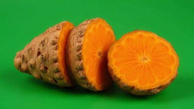 Fresh turmeric root sliced into three pieces against green background