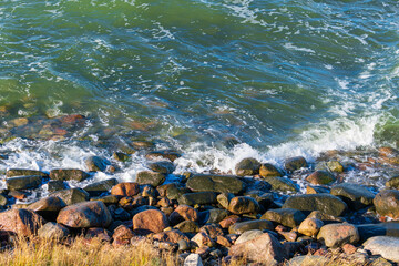 Rocky Shoreline with Rough Ocean Waves Crashing on Wet Boulders in Beautiful Warm Sunlight. Natural Coastal Landscape with Green Blue Sea Water Splashing Over Stone Beach on a Bright Sunny Day © Aimur
