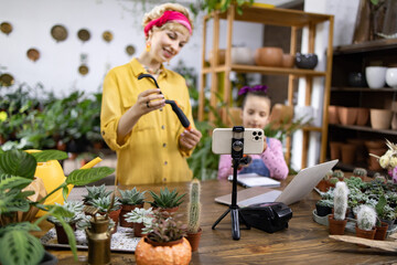 A woman and child are filming a plant care tutorial in a bright, inviting plant shop setting