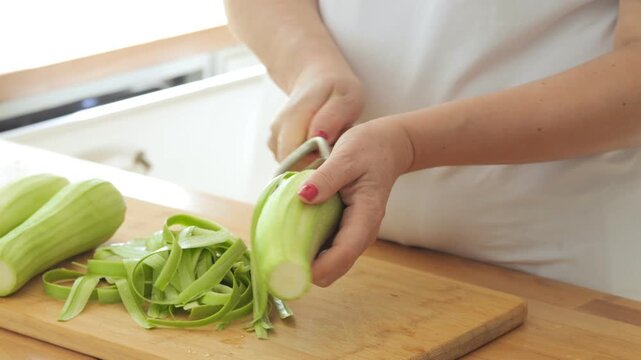 Woman is cutting a cucumber with a mandolin. She is wearing a red shirt