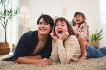 Happy Asian family lying and laughing together on carpet at home