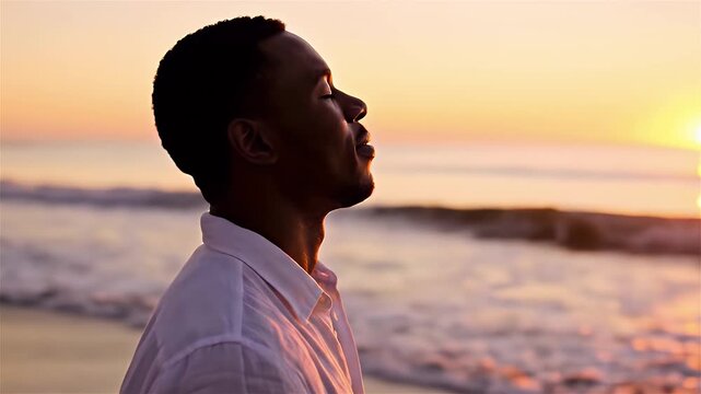 A man stands on a serene beach at sunset, breathing deeply and relaxing. The calm person enjoys fresh air outdoors during his summer vacation.