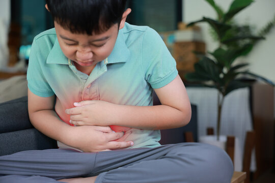 Asian boy holding belly suffering from severe abdominal pain with red inflamed area. Concept of stomach ache, indigestion, food poisoning, gastritis, and pediatric medical healthcare treatment.
