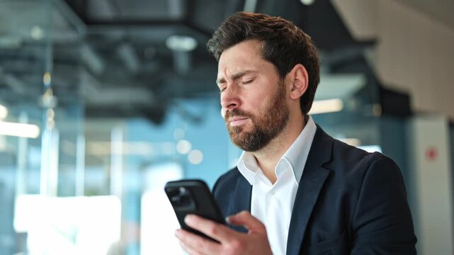 Business professional looking at smartphone, expressing confusion, worry, and disappointment. Receiving distressing news, reacting with stress and sadness in a modern office.