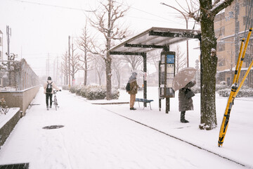 雪が降る中バスを待つ人