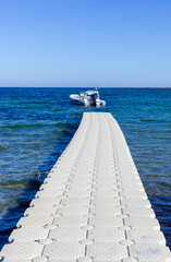 Fototapeta premium Boat docked at floating pier in the Mediterranean Sea. Clear blue water with summer sky. Sardinia, Italy, coastal scenery with turquoise horizon.