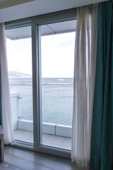 Fototapeta premium Cozy hotel room interior with sofa and table set with wine and fruit, overlooking marina and sea through large window.