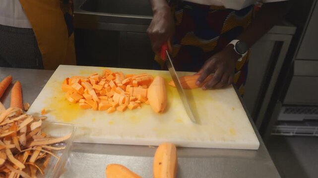 African woman chef chopping yam into cubes on cutting board for velout&eacute; soup preparation in kitchen