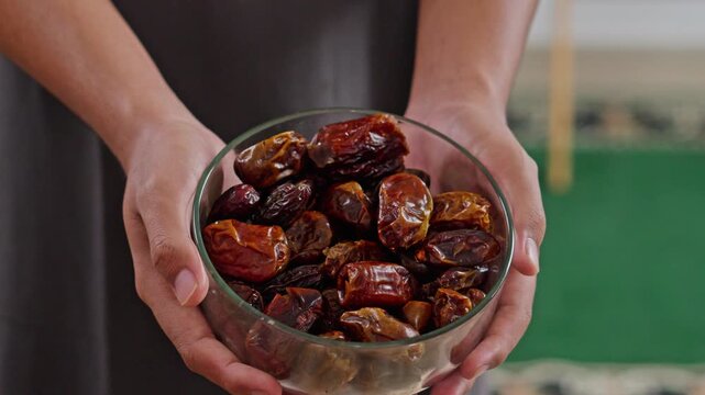 Close-up of Hands sharing dried dates from glass bowl during religious or cultural gathering