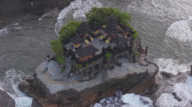 High angle view of the iconic tanah lot temple, a hindu shrine built on a rocky islet with waves crashing against its shores in bali